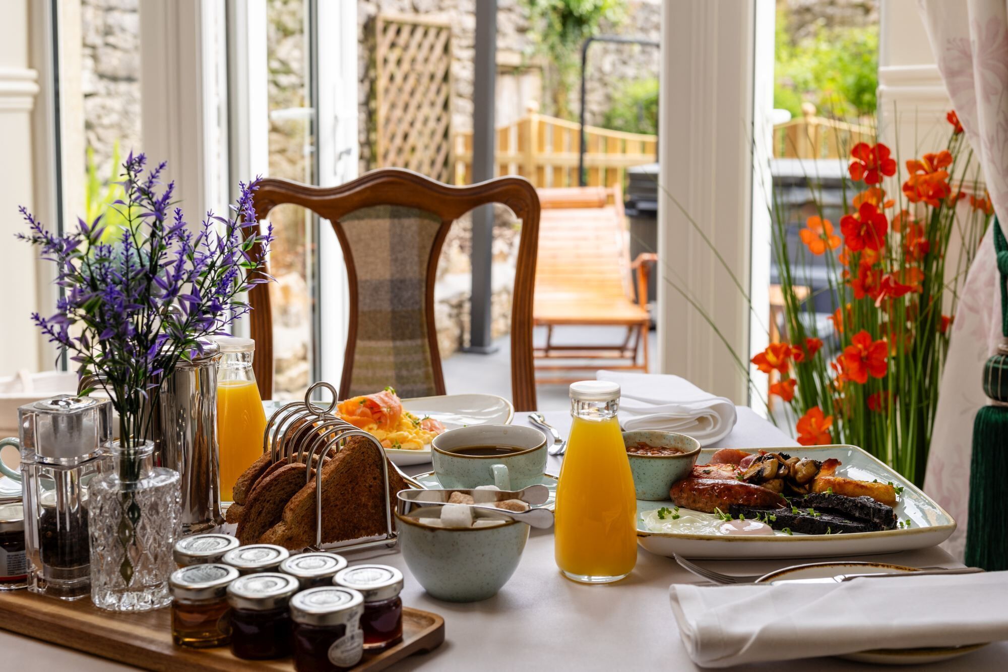 A breakfast table with various food items, condiments, and a view of the outdoors.