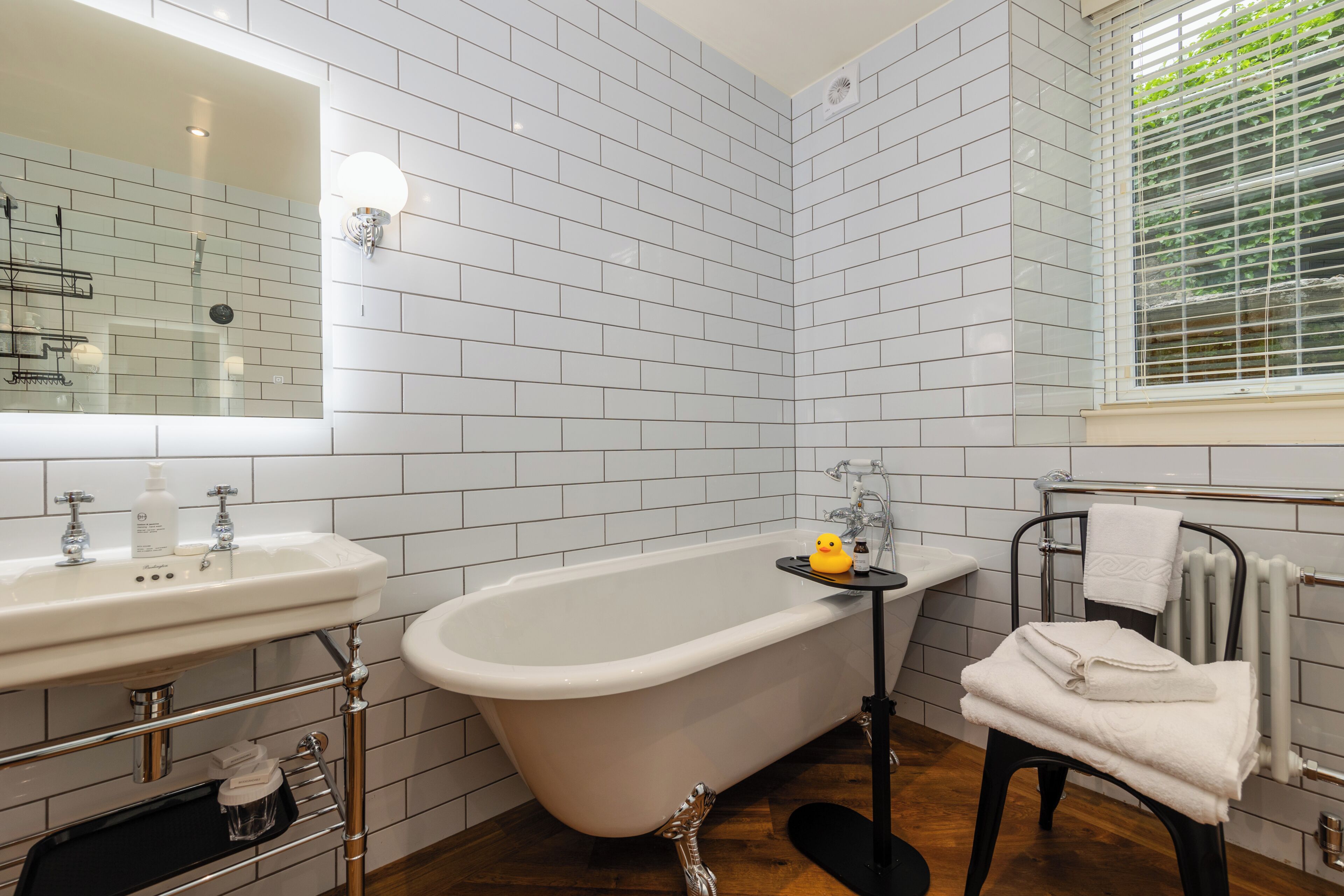 A bathroom with white subway tiles, a freestanding bathtub, a sink with a mirror, and a towel rack.