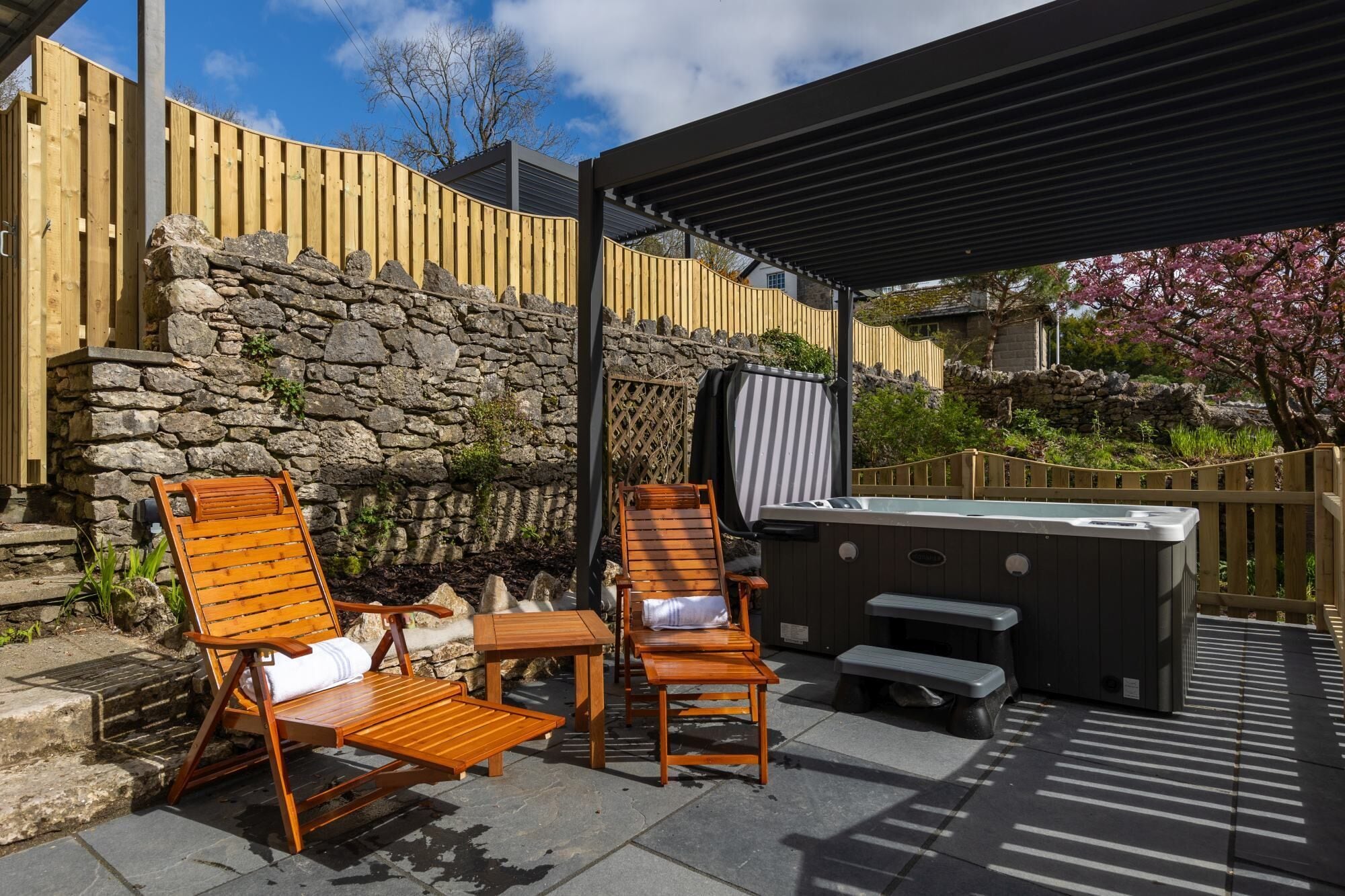 An outdoor patio with wooden chairs, a hot tub, and a stone wall.