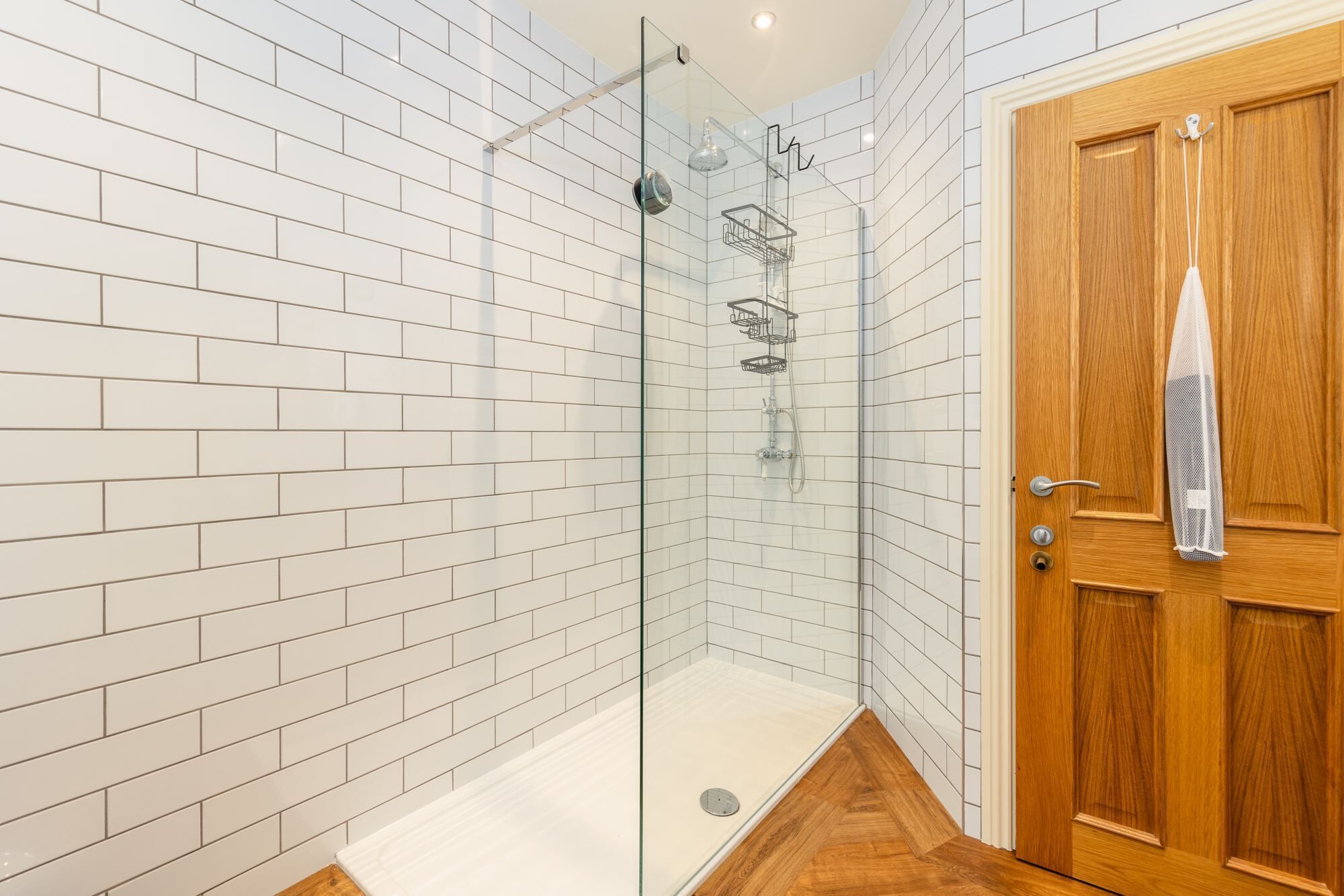 A modern bathroom with a glass-enclosed shower, white tiled walls, and a wooden door.