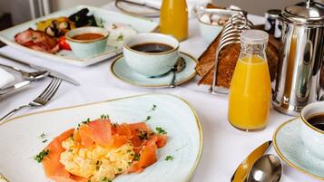 A breakfast setting with plates of smoked salmon and scrambled eggs, a bottle of orange juice, and a coffee pot.