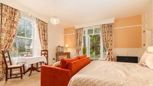 A bedroom with a bed, a desk, and a chair. There are windows with curtains. - Grange Manor (Grange-over-Sands)