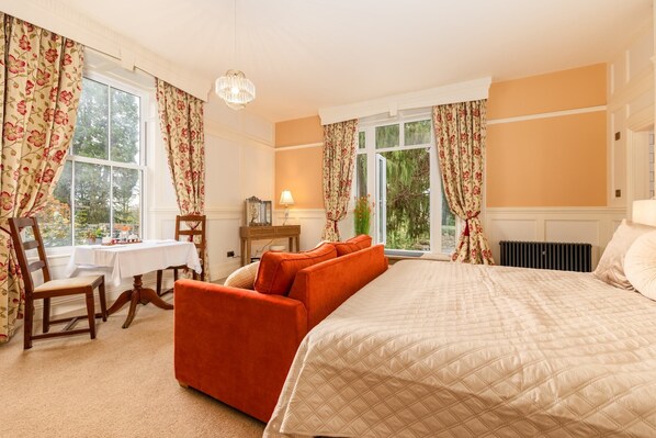 A bedroom with a bed, a desk, and a chair. There are windows with curtains. - Grange Manor (Grange-over-Sands)