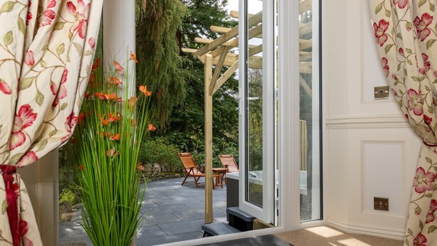 A room with a view of a garden through a glass door, a wooden chair, and a potted plant. - Grange Manor (Grange-over-Sands)
