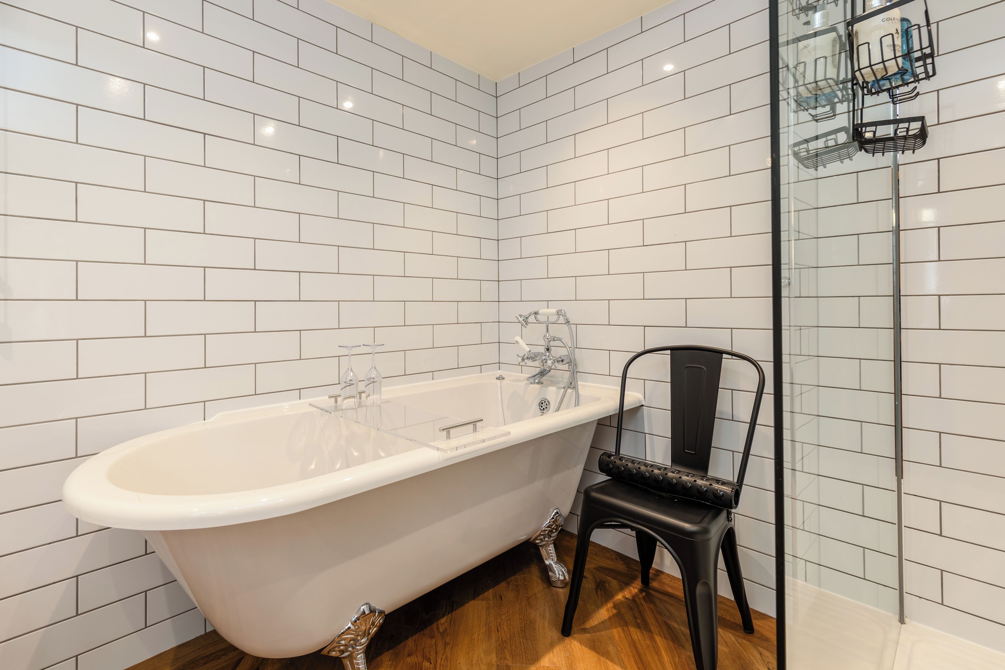 A bathroom with a freestanding bathtub, a glass shower enclosure, and a black chair.