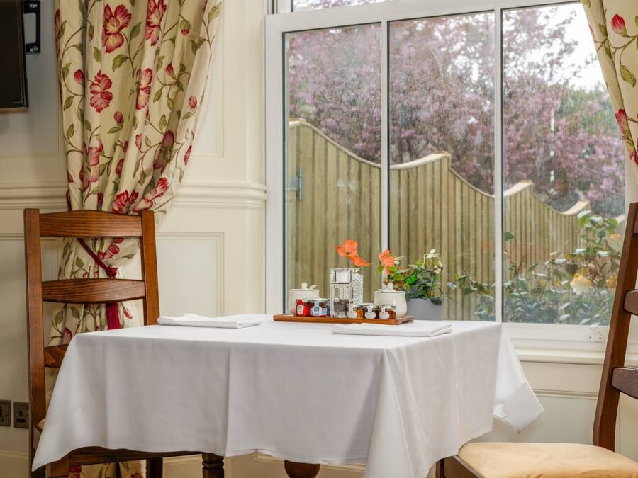 A dining area with a table set for two, a wooden chair, and a window with a view of a garden.