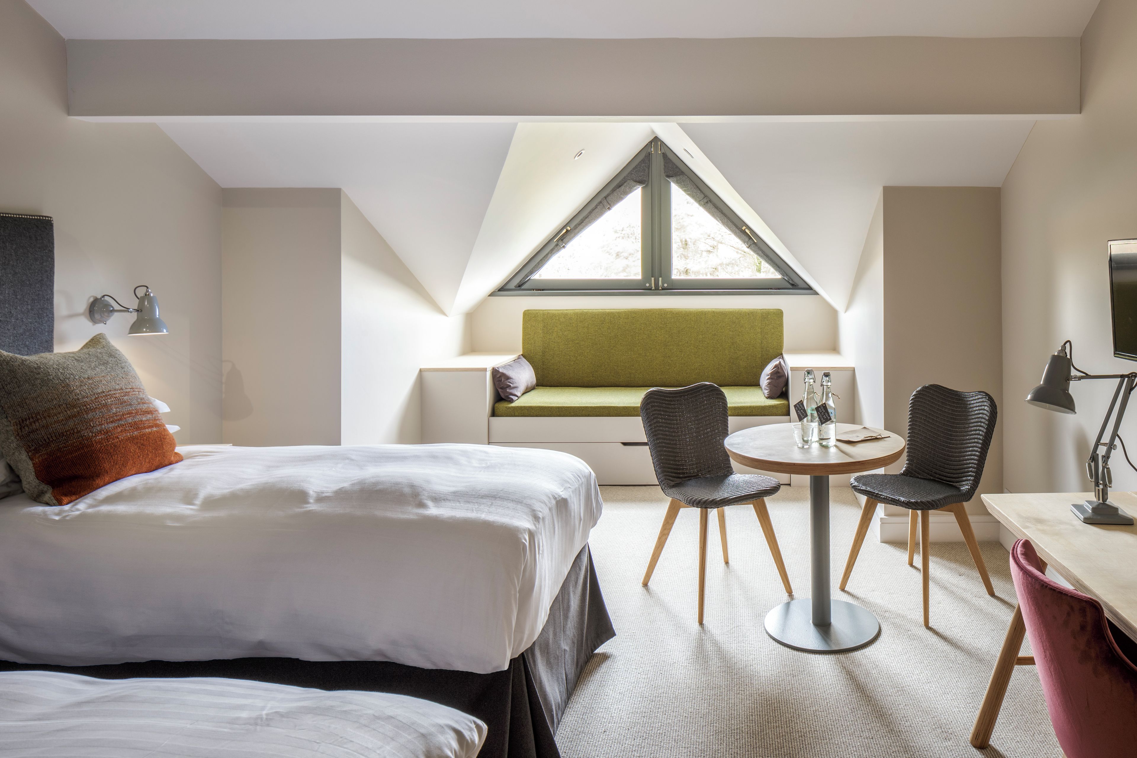 Une chambre d’hôtel moderne avec un lit, un canapé vert, deux fauteuils, une petite table et un téléviseur.