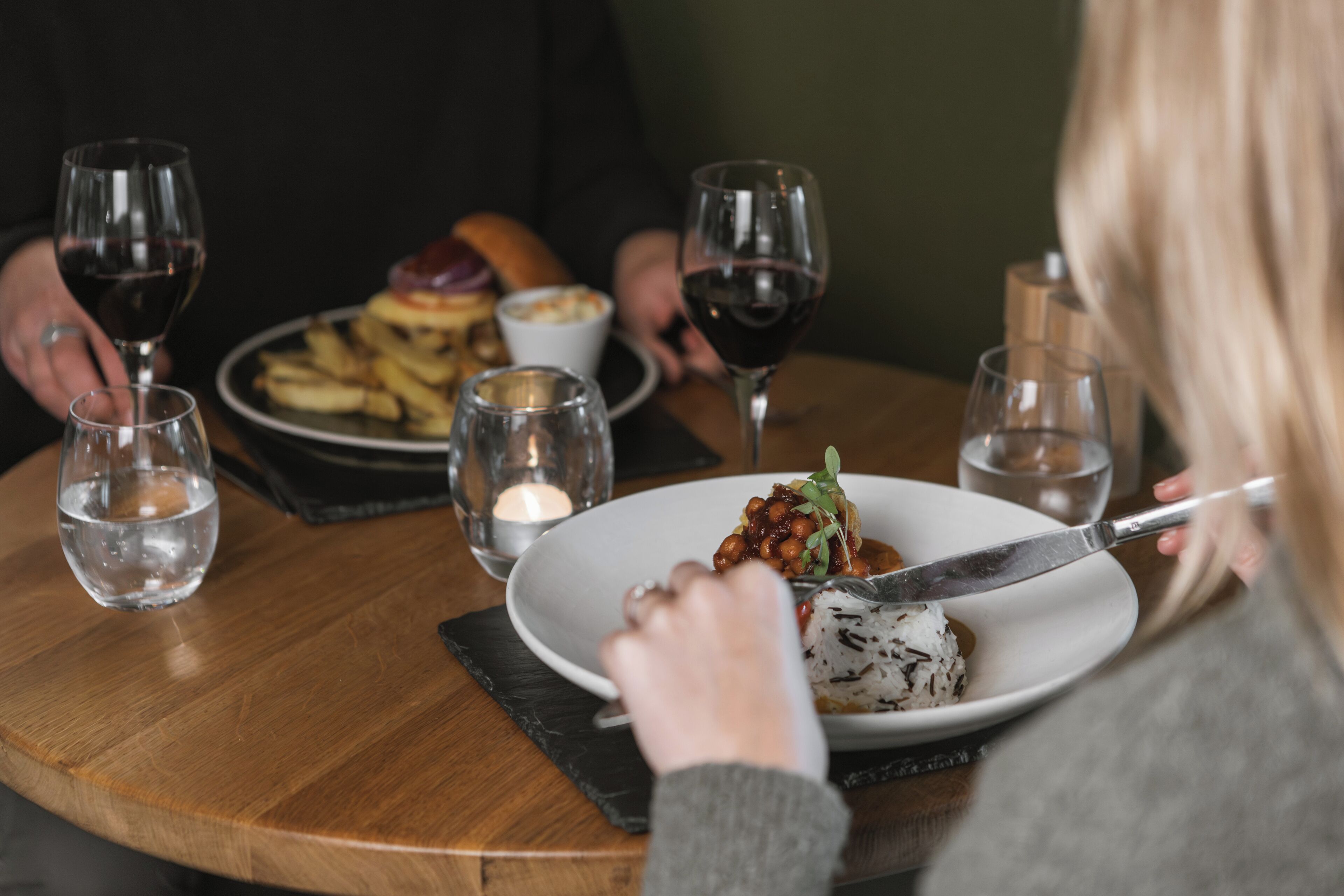 A dining table with plates of food, glasses of wine, and a candle.