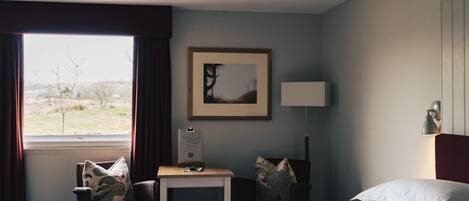 A hotel room with a bed, a desk, a chair, a lamp, and a window with curtains.