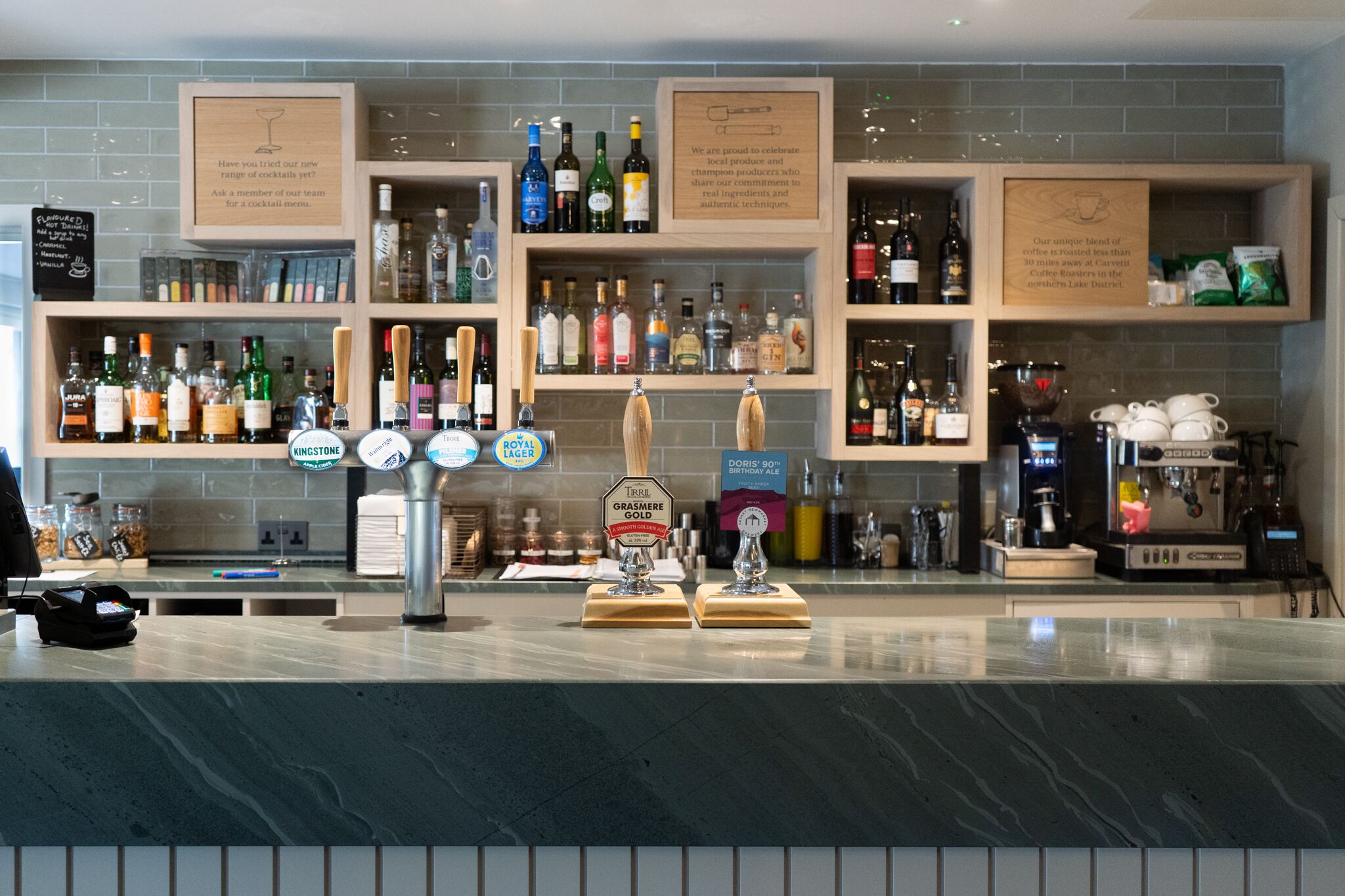 A bar area with multiple shelves of bottles, a coffee machine, and two beer taps.