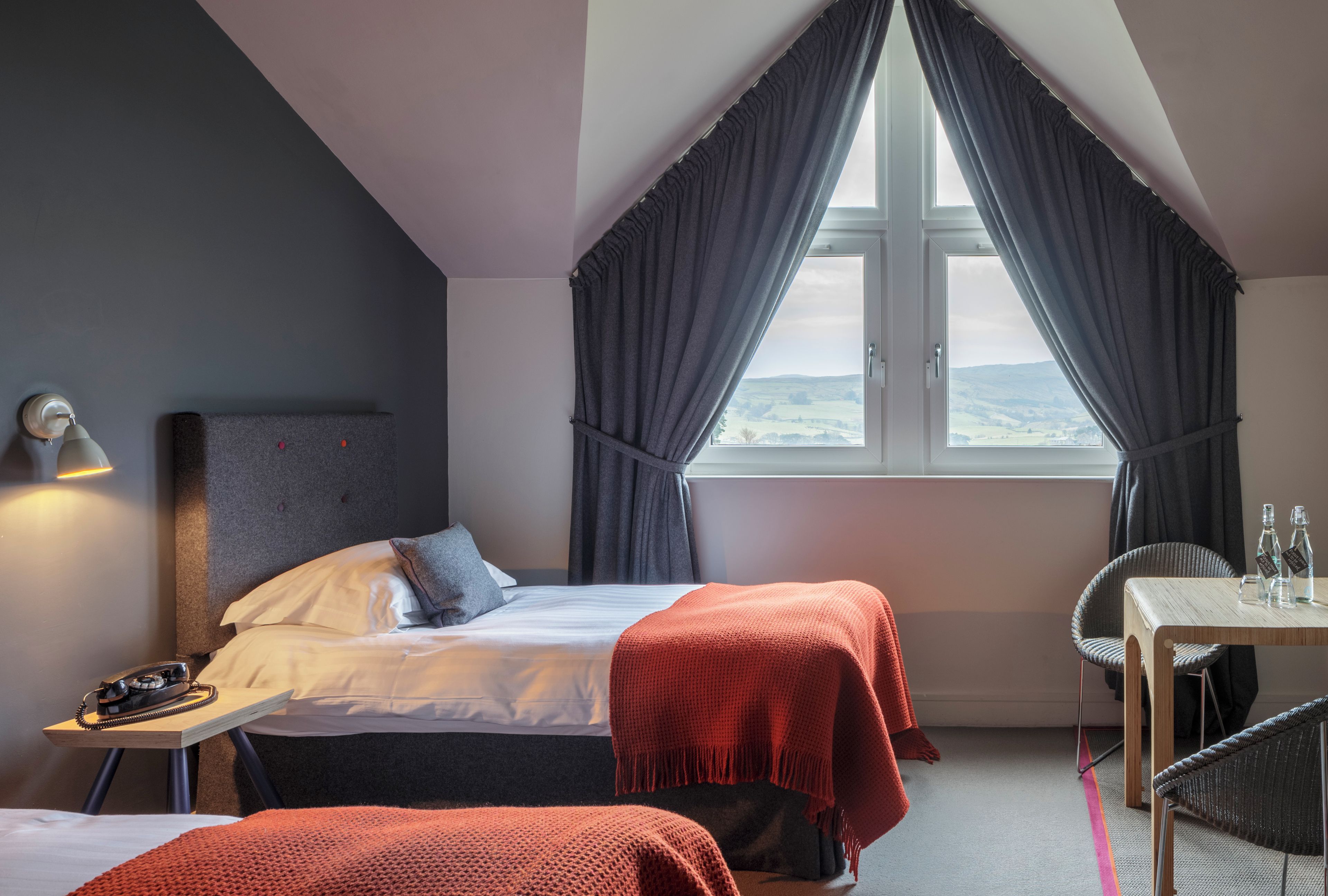A bedroom with a bed, bedside table, lamp, and a view of the outdoors through a window.