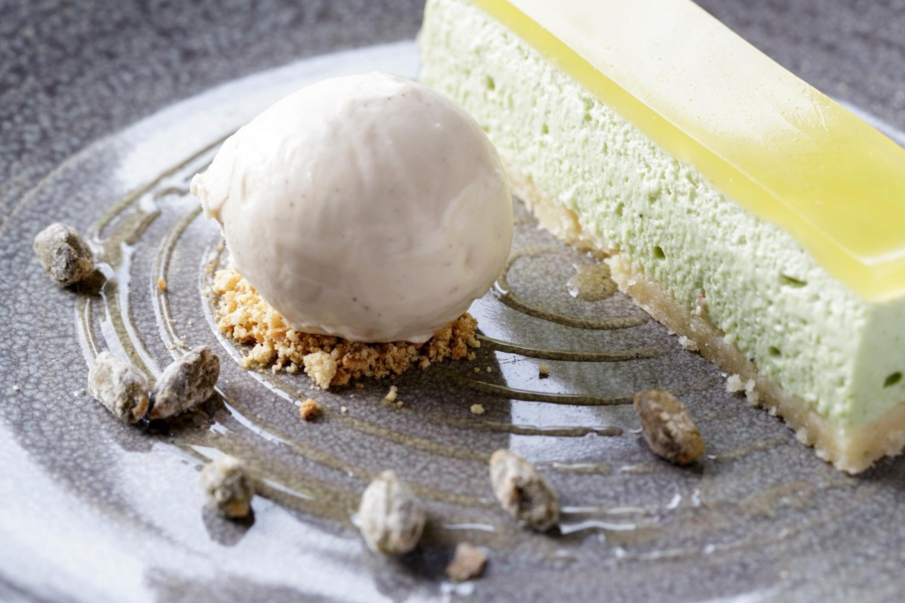 A dessert plate with a scoop of ice cream, a slice of cheesecake, and scattered nuts.