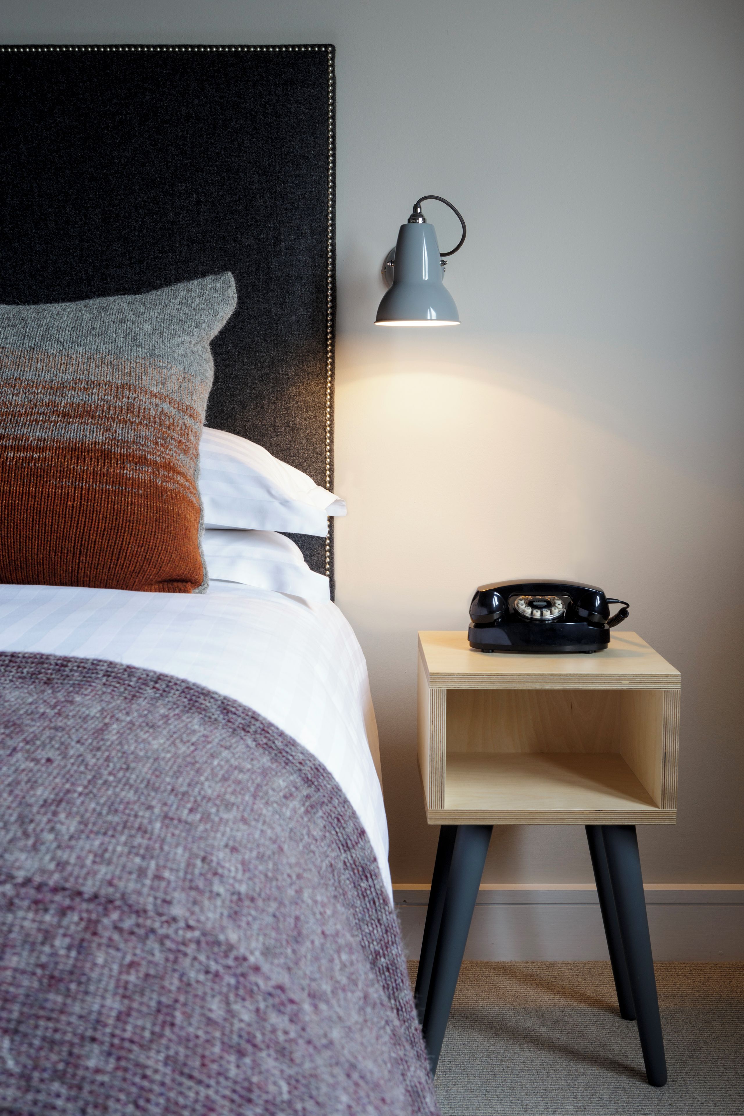 A neatly made bed with a headboard, a bedside lamp, and a telephone on a small wooden nightstand.