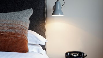 En snyggt bäddad säng med en sänggavel, en sänglampa och en telefon på ett litet träbord bredvid sängen.