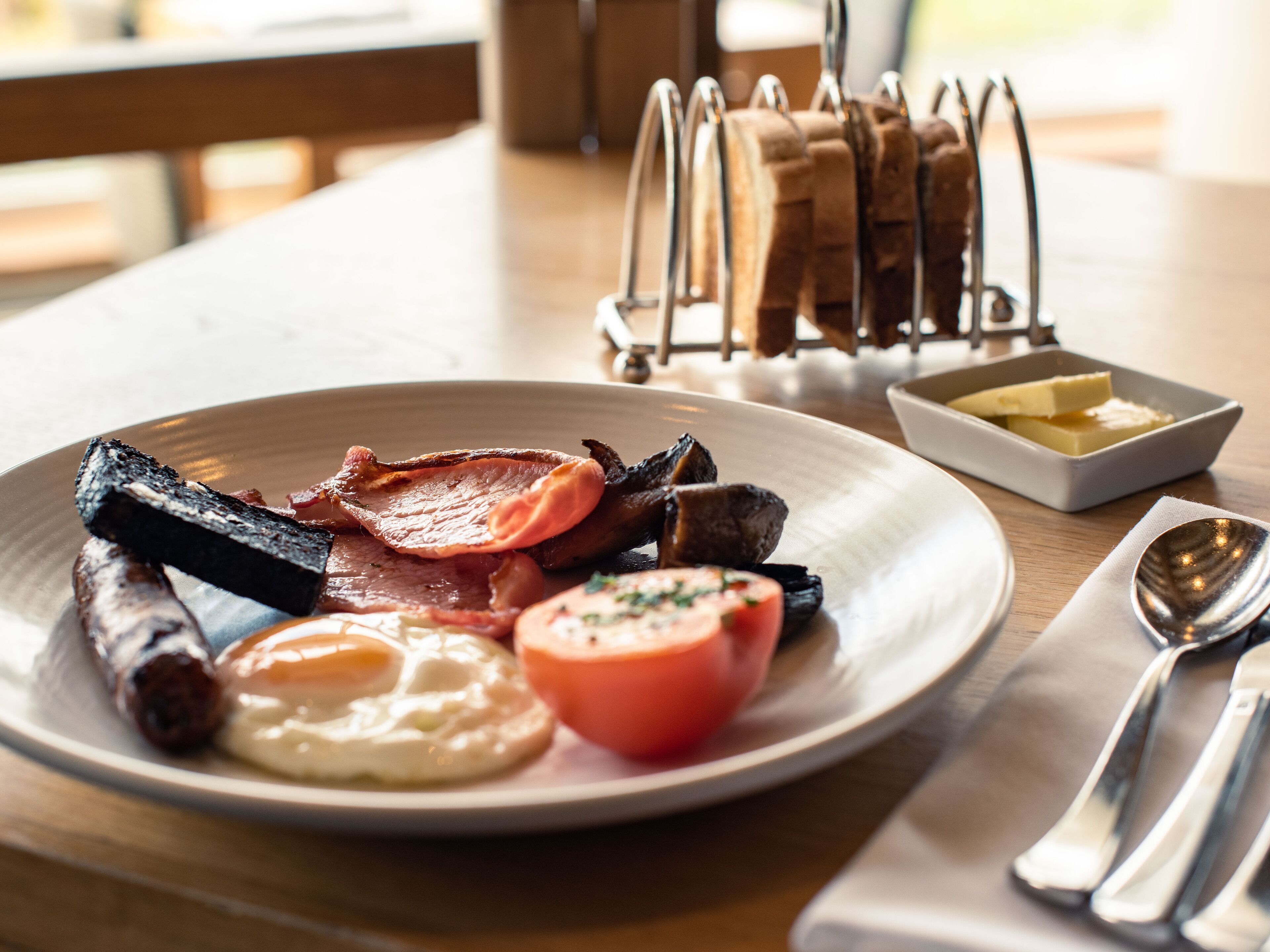 A breakfast plate with bacon, sausages, eggs, and tomatoes on a wooden table.