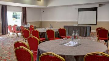 A conference room with round tables, red chairs, and a projector screen.