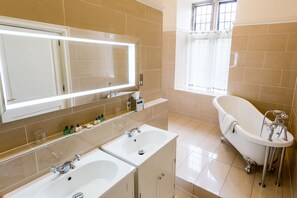 A bathroom with two sinks, a large mirror, and a clawfoot bathtub.