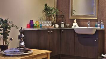 A corner of a room with a wooden table, a mirror, a sink, and cabinets.