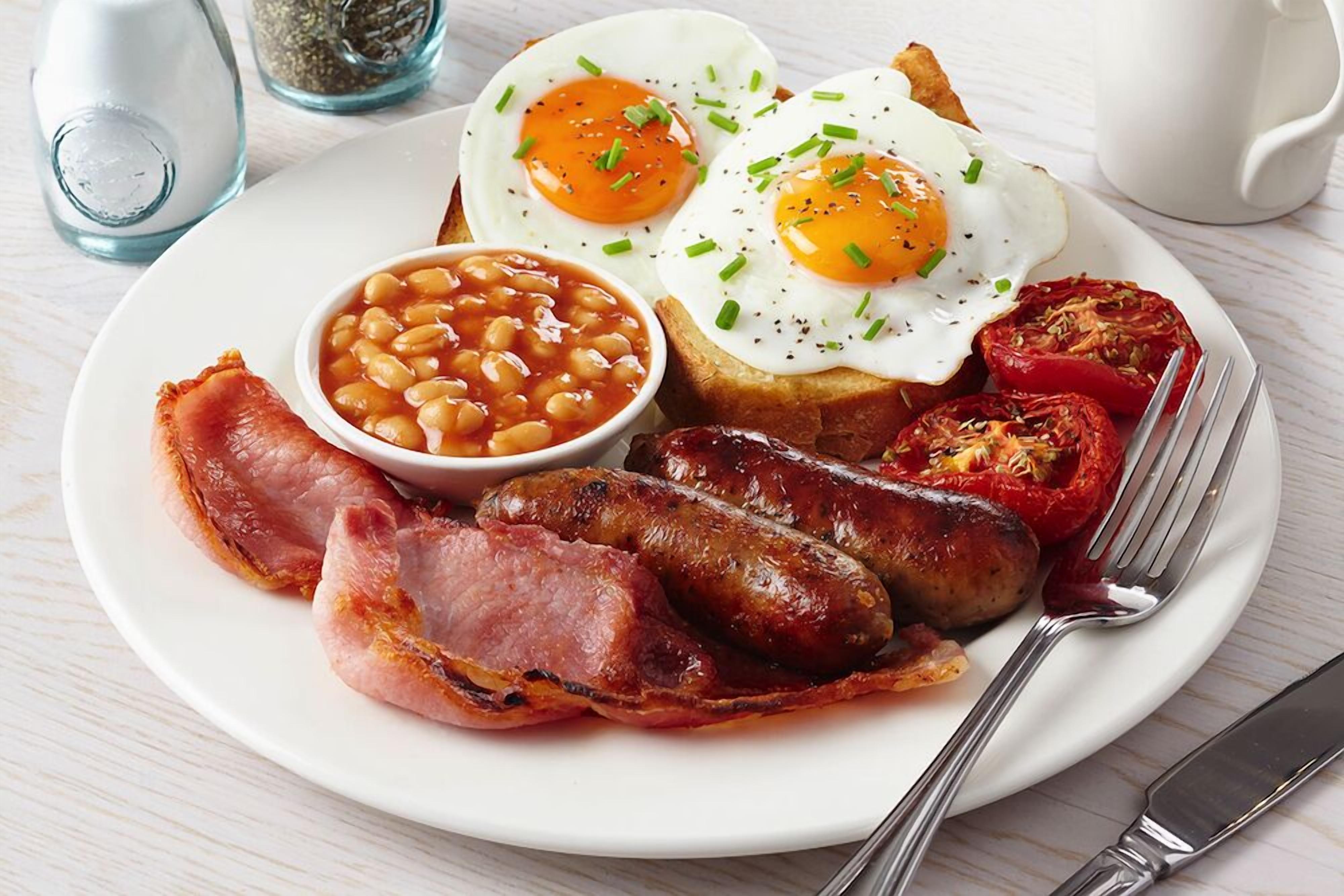 Un plato con huevos, frijoles, salchichas, tocino y tomates.