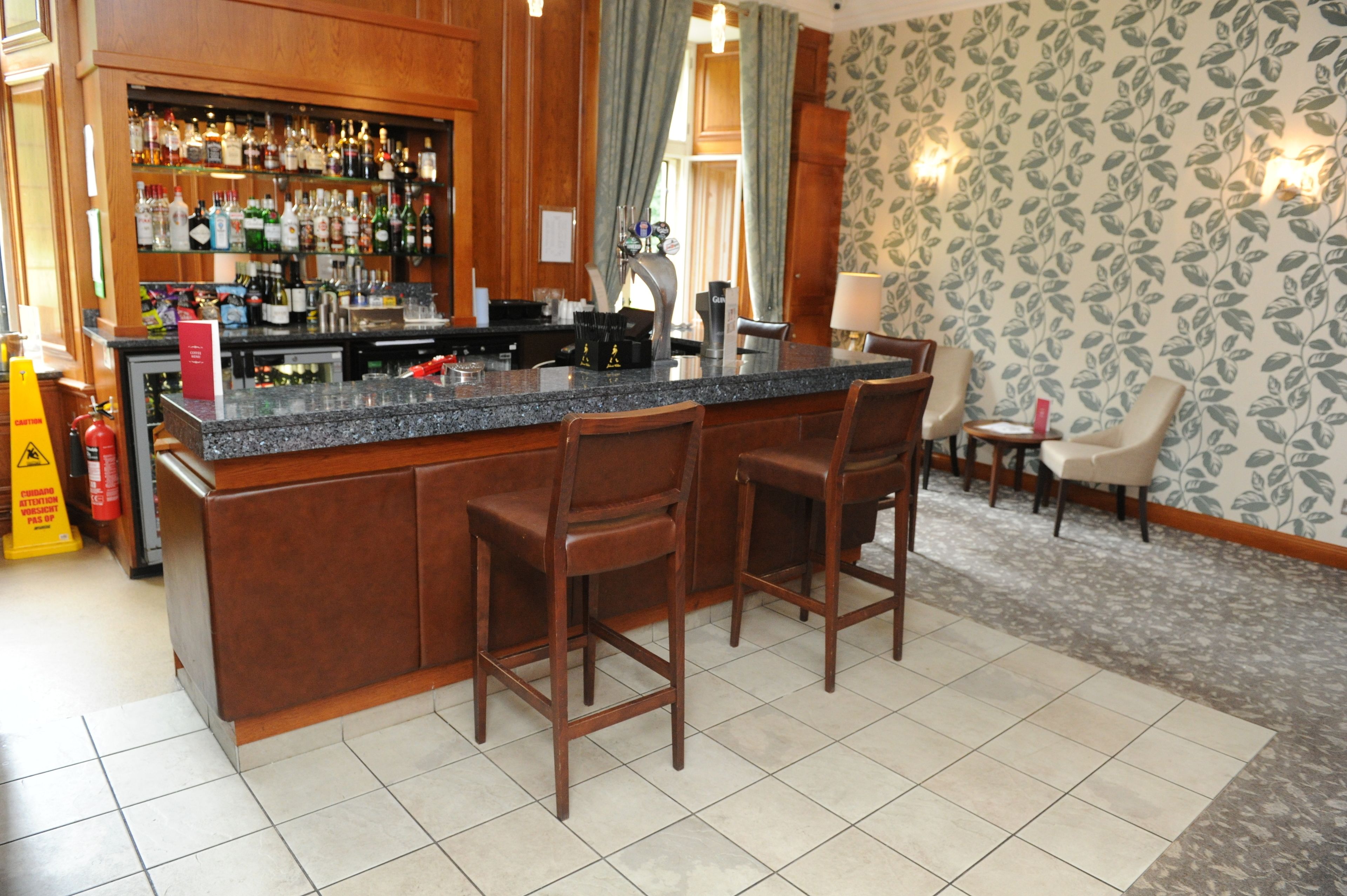 A bar area with a granite countertop, wooden bar stools, and a variety of liquor bottles.