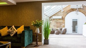 A modern living room with a green sofa, decorative pillows, a tall vase with green plants, and a unique wooden table. - Hellaby Hall Hotel, BW Signature Collection (Rotherham)