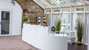 A reception area with a stone wall, a white reception desk, and a glass enclosure with plants. - Hellaby Hall Hotel, BW Signature Collection (Rotherham)