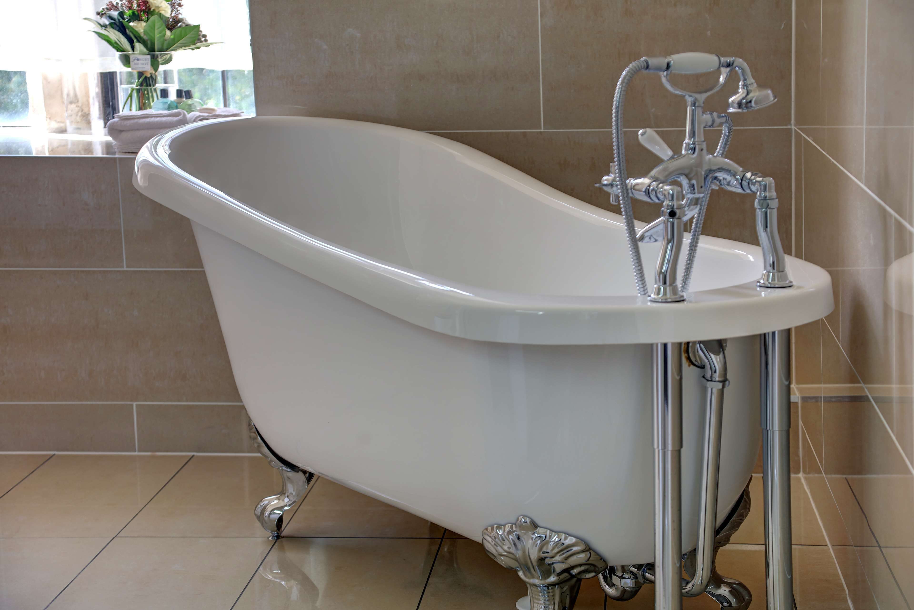 A clawfoot bathtub in a bathroom with beige tiles and a window with flowers.