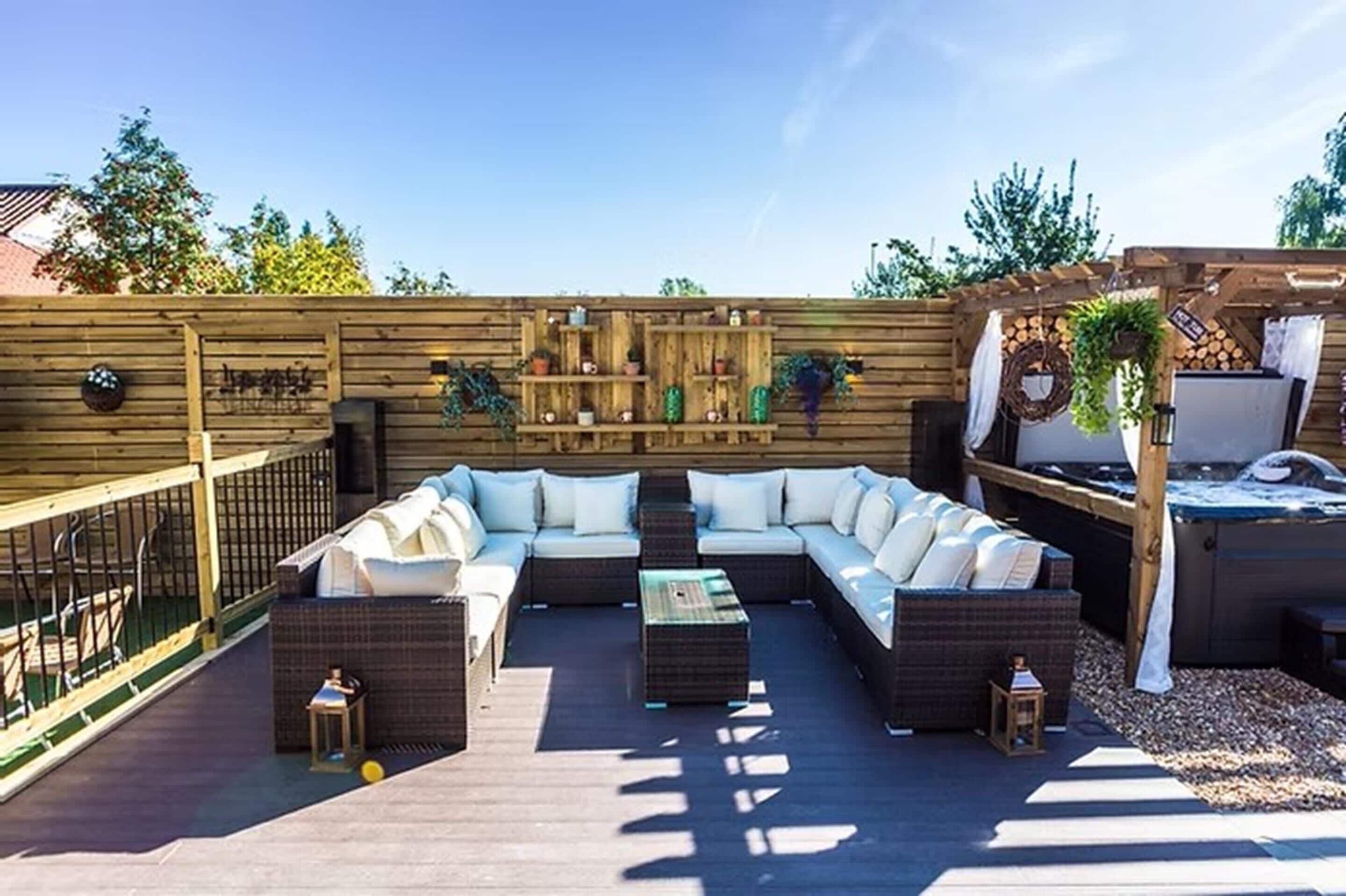 An outdoor patio with a sectional sofa, a small table, and a wooden wall with shelves.