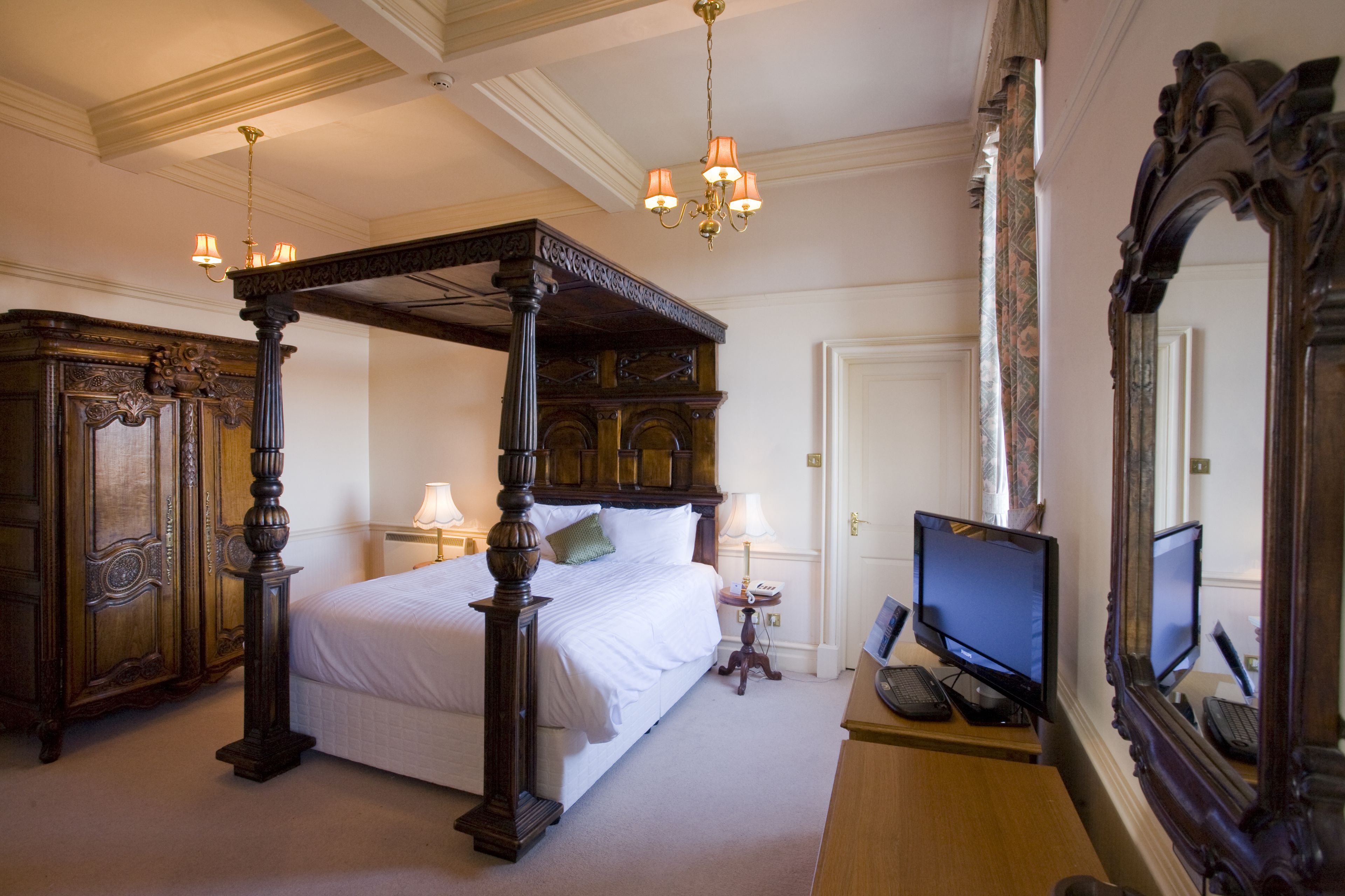 A four-poster bed with a wooden frame, a desk with a computer, and a large mirror.