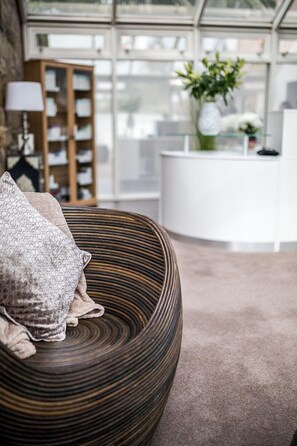A modern living room with a round, textured sofa, a wooden bookshelf, and a white reception desk. - Hellaby Hall Hotel, BW Signature Collection (Rotherham)