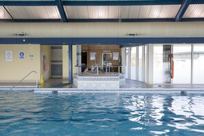 Une piscine intérieure offrant une vue dégagée sur l’ensemble de l’espace piscine, avec un plongeoir et un poste de surveillance pour les sauveteurs.