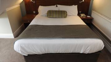 A hotel room with a large bed, a wooden headboard, a bedside table with a lamp, and a telephone.