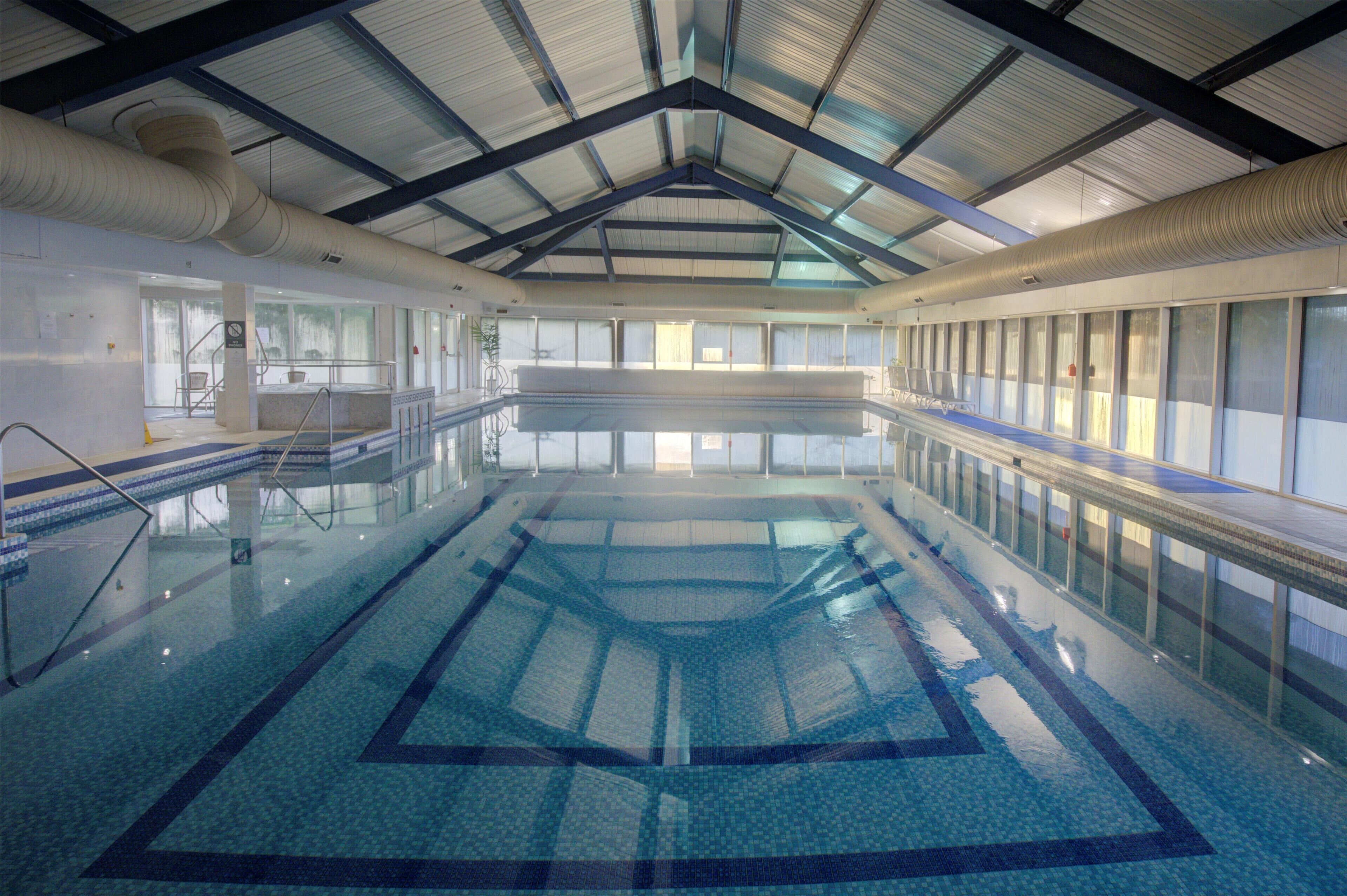 Una piscina interior con agua cristalina, suelo de baldosas y techo alto con vigas de metal.