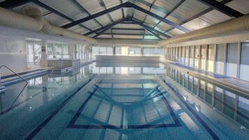 Una piscina interior con agua cristalina, suelo de baldosas y techo alto con vigas de metal.