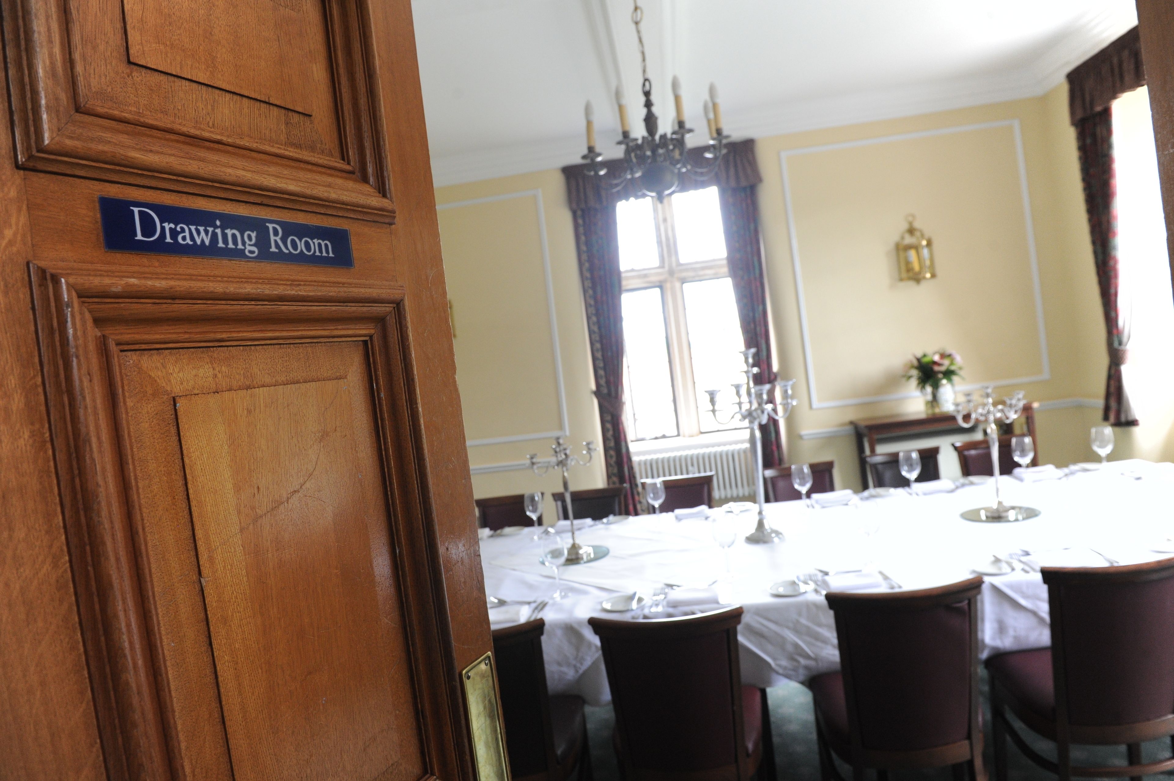 A dining room with a table set for six, a chandelier, and a window with curtains.