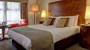 Een hotelkamer met een groot bed, twee bedlampen, een rode fauteuil en een kleine tafel met een waterkoker.