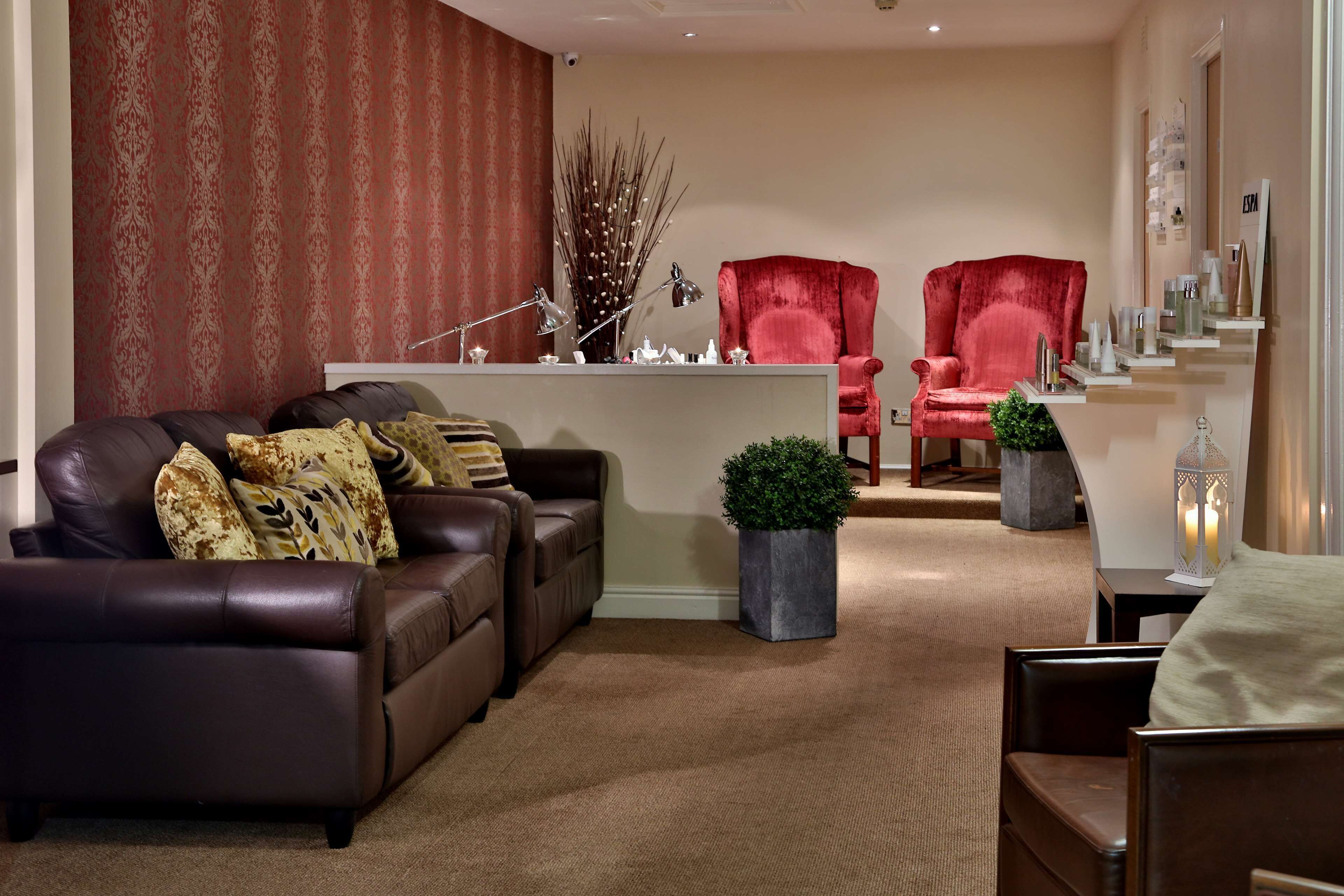 A living room with a brown leather sofa, two red armchairs, a small coffee table, and a decorative plant.