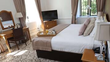 A hotel room with a bed, a desk, a television, and a tray with breakfast items.