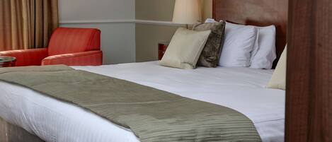 Una habitación de hotel con una cama grande, un sillón rojo, una mesita de noche y una lámpara.