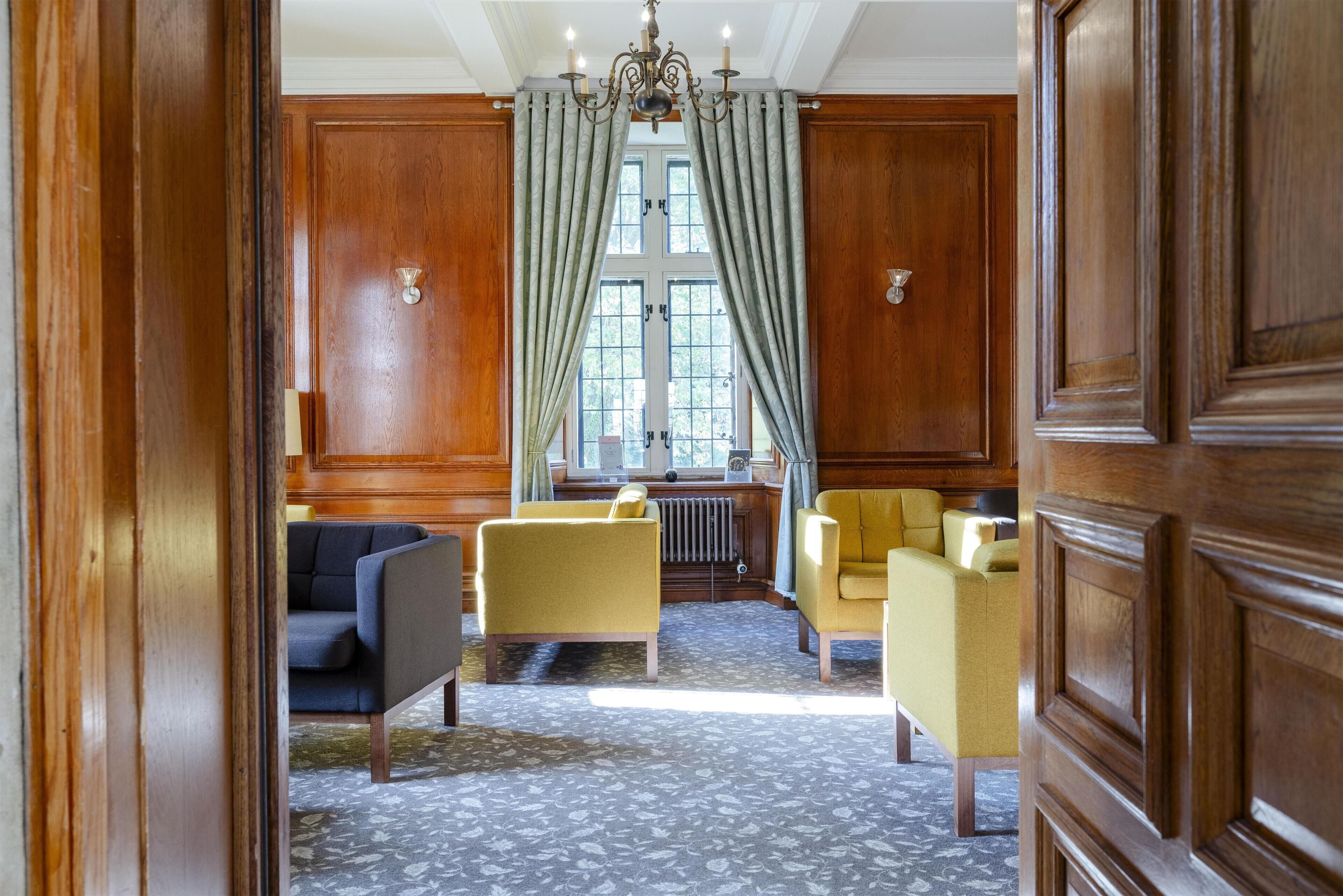 A room with a large wooden door, a window with curtains, a radiator, and two armchairs.