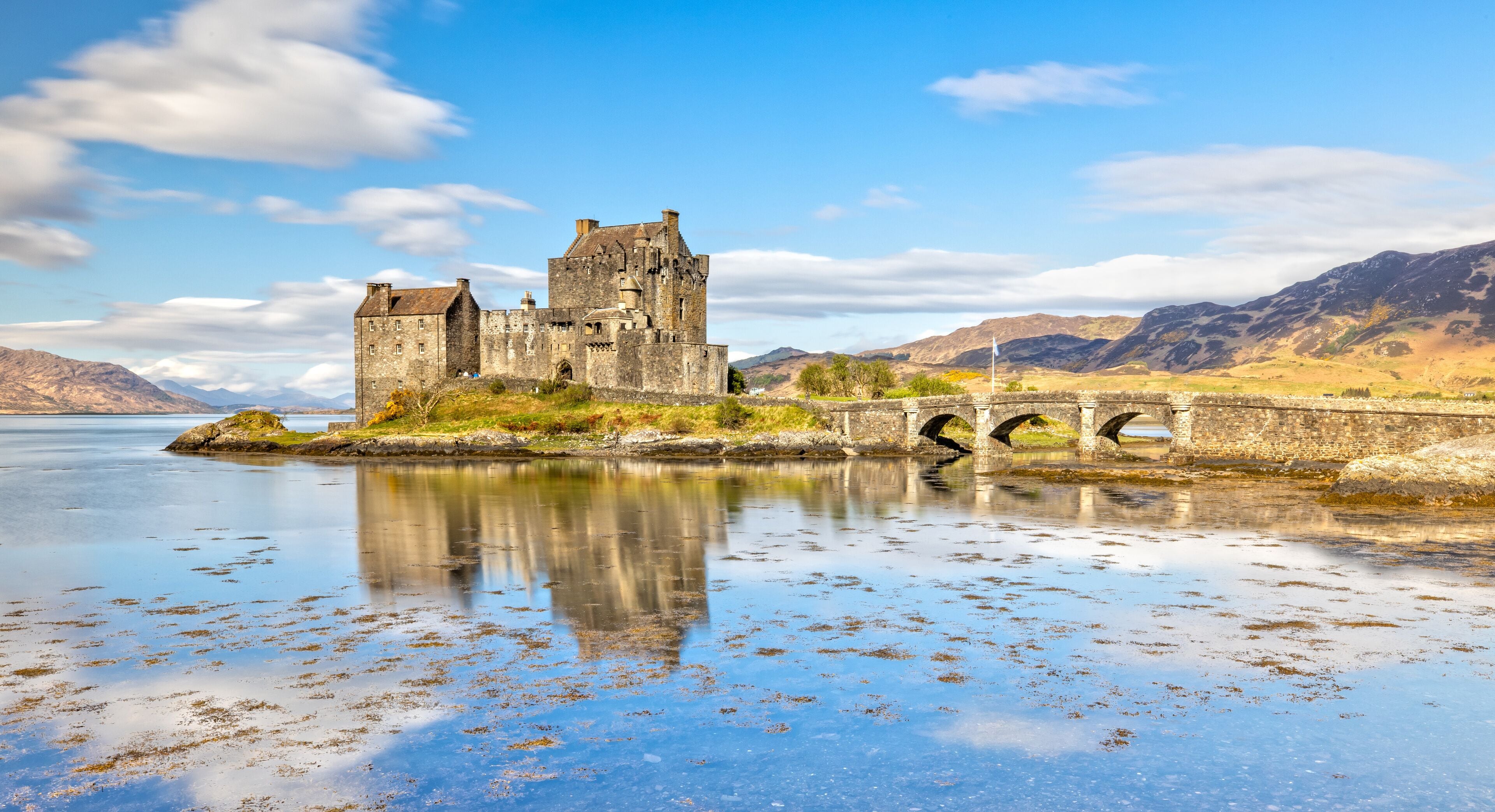 A historic castle by a calm lake with a stone bridge.