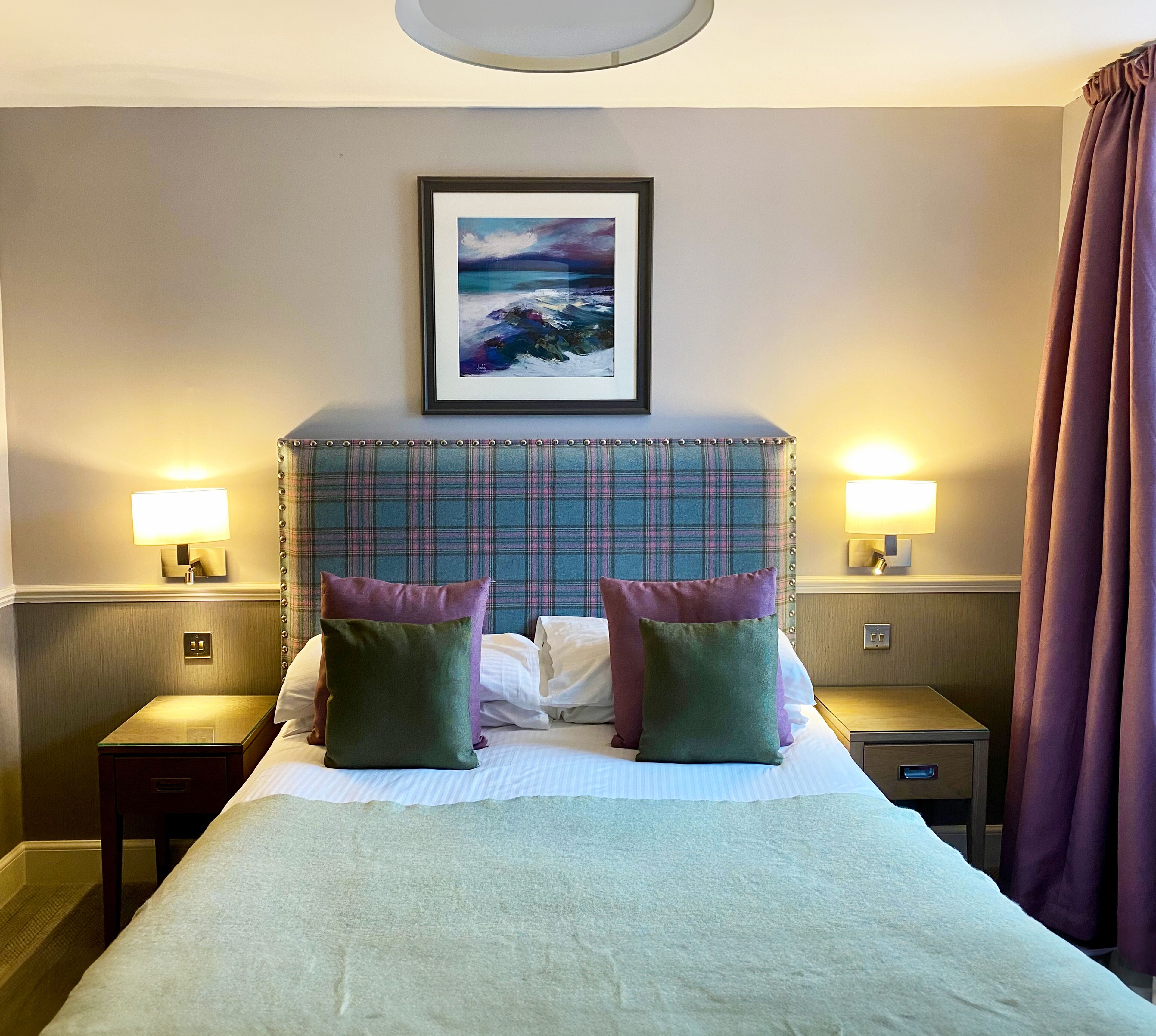 Camera d'albergo con un letto grande, due comodini con lampade, un quadro appeso alla parete e una finestra con tende.