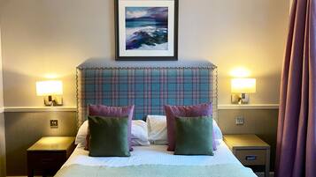 Une chambre d’hôtel avec un grand lit, deux tables de chevet avec des lampes, un tableau encadré au mur et une fenêtre avec des rideaux.