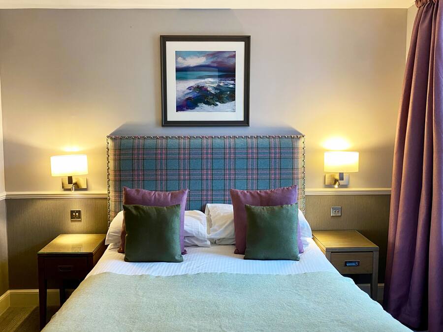 Une chambre d’hôtel avec un grand lit, deux tables de chevet avec des lampes, un tableau encadré au mur et une fenêtre avec des rideaux.