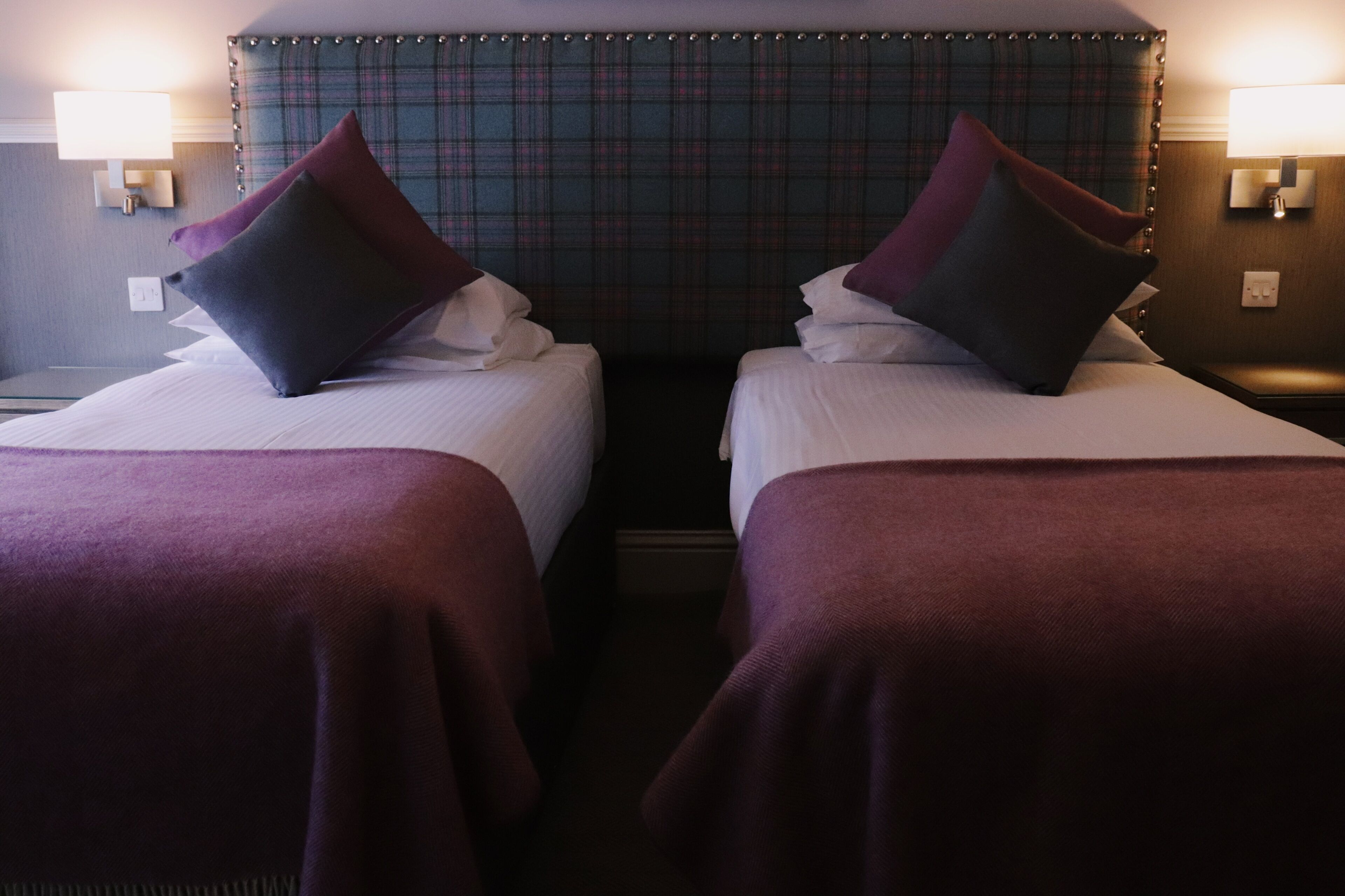 Two beds with headboards, a plaid headboard, and wall-mounted lamps.