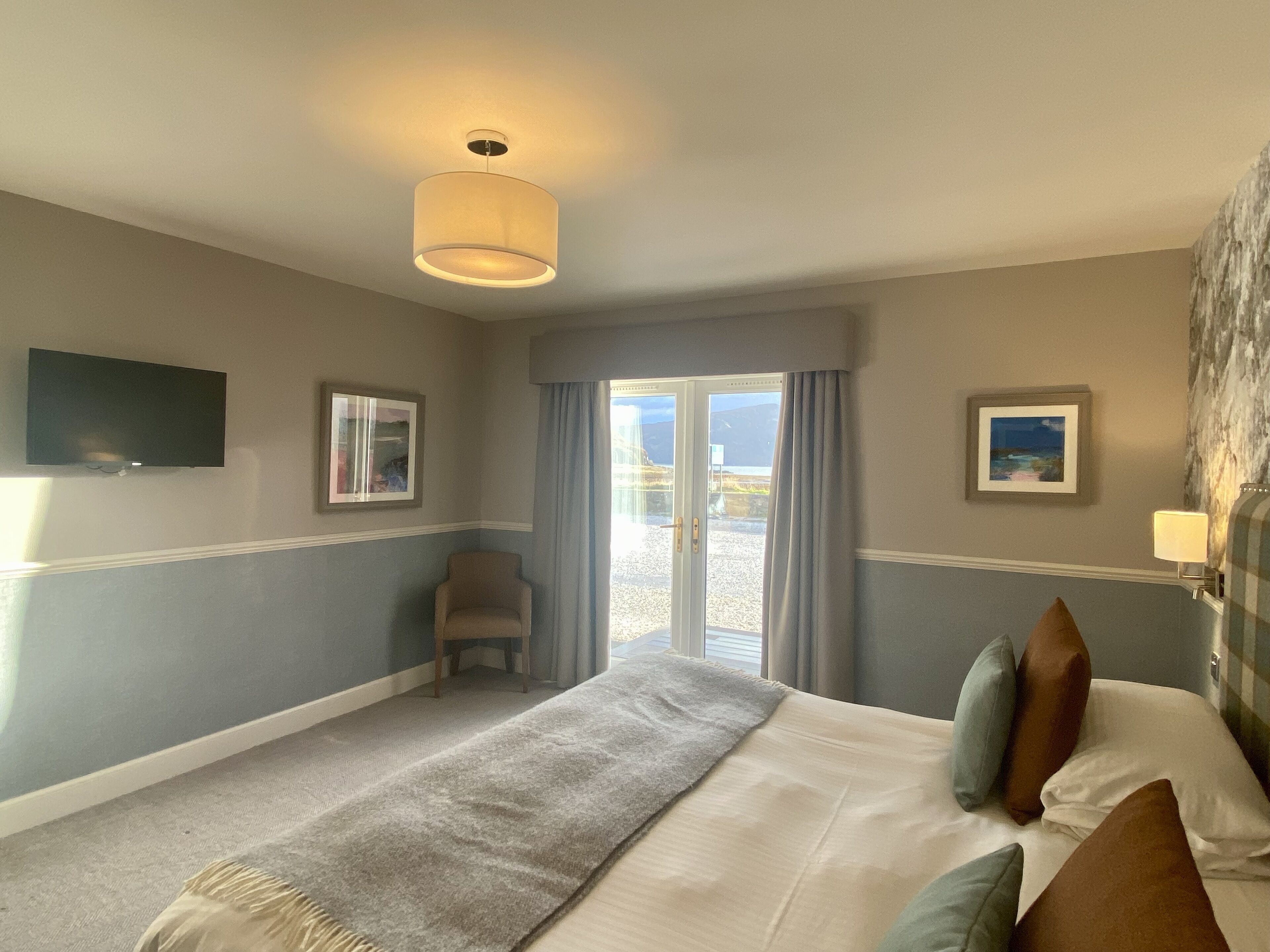 A hotel room with a bed, a chair, a television, and a window with curtains.