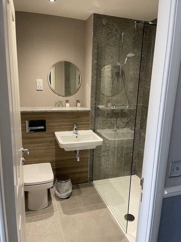 Un baño moderno con inodoro, lavamanos y ducha con mampara de vidrio.