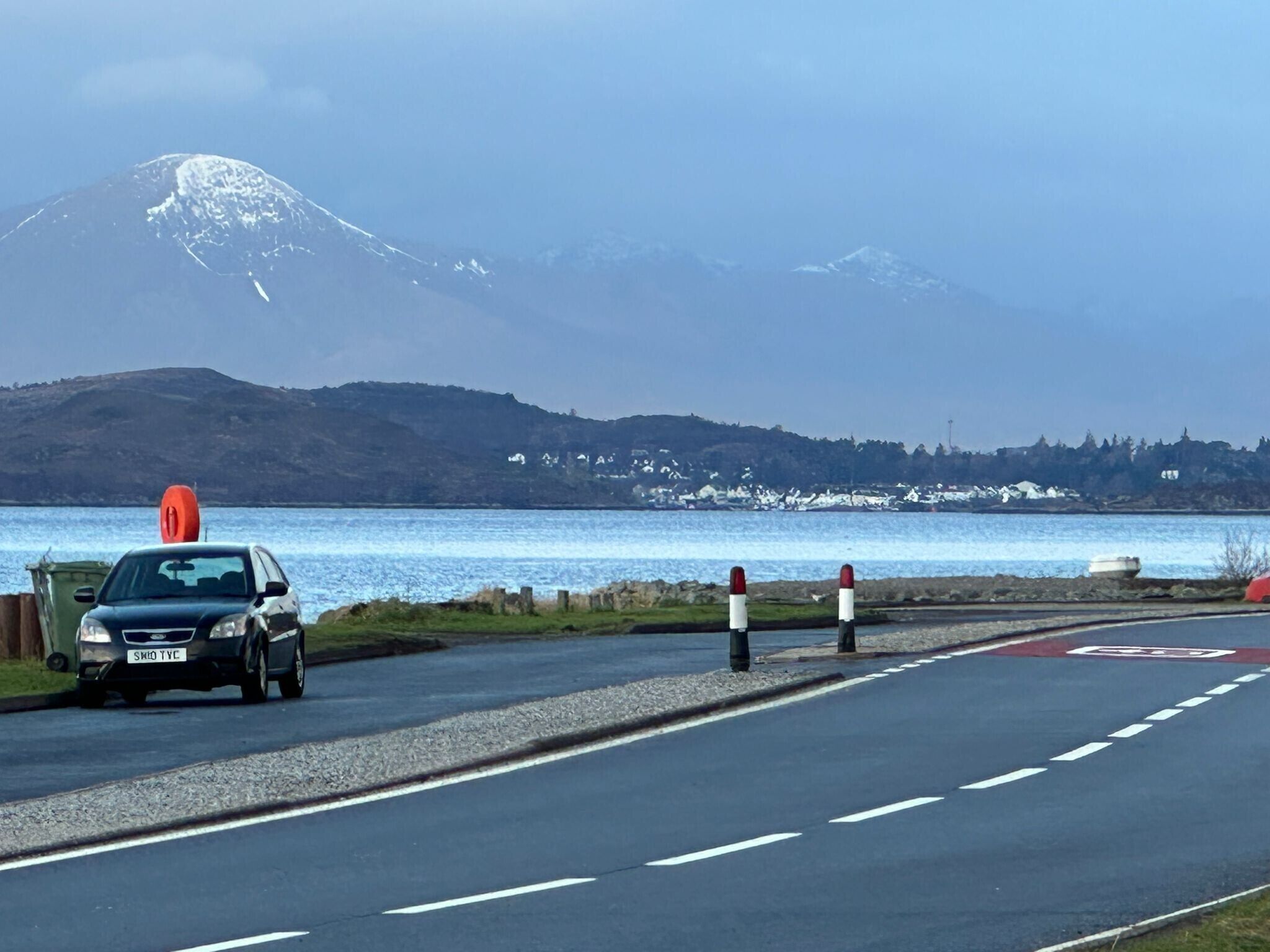 A road with a car, a mountain in the background, and a body of water.