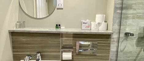 A modern bathroom with a white sink, a mirror, a towel dispenser, and a glass shower enclosure.