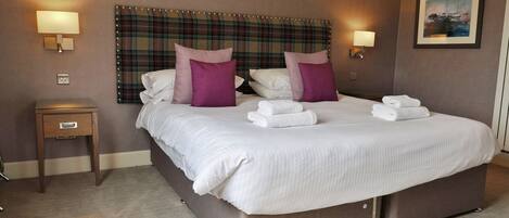 A hotel room with a large bed, two bedside lamps, a small bedside table, and a painting on the wall.